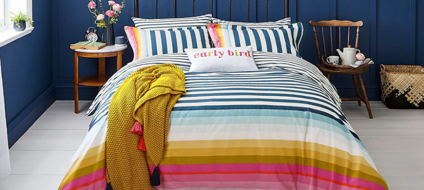 Joules Cambridge Stripe bedding: A large-striped duvet cover set with a predominantly white and navy pattern, morphing in to light blue, mustard and pink stripes towards the bottom of the duvet cover and one side of the pillowcases.