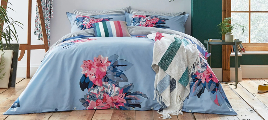Joules Cornish Floral bedding: A light blue duvet set featuring a large pink and navy floral pattern, with contrasting white and navy horizontal stripes on the reverse.