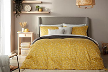 A double bed dressed in a yellow duvet cover, with matching and contrasting white pillowcases.