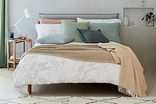 A bed dressed in a white and charcoal leaf print design, with a range of plain, pastel coloured accessories.