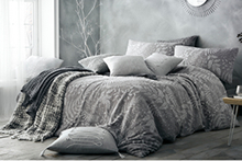 A cosy-looking double bed dressed in a grey patterned duvet cover, with a range of contrasting cushions and throws scattered upon it.