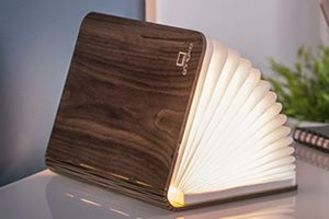 A stylish wooden book shaped light, partially open, with a warm white light glowing from within the pages.
