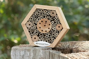 A simple hexagonal insect house with a sturdy wooden frame, tightly packed with a range of small wooden tubes of various thicknesses.